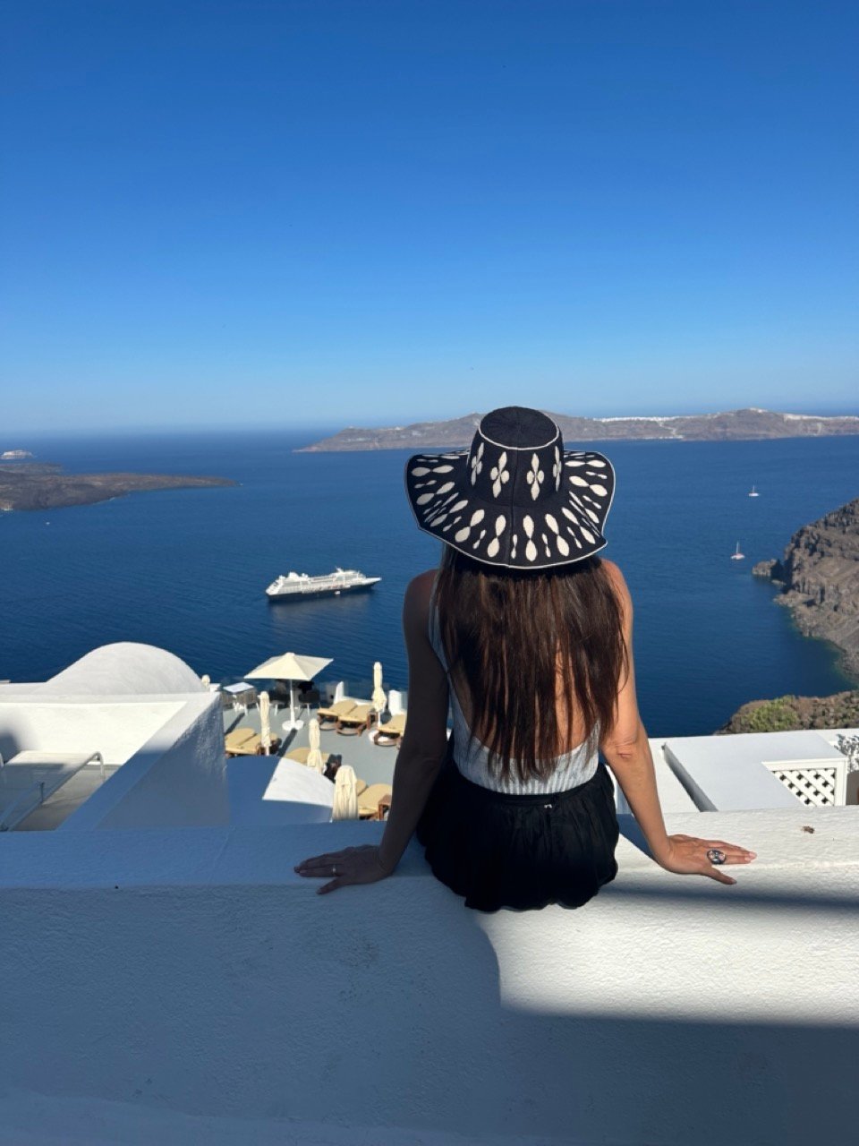 A lady watches the greek sun, sea and sky full of inspiration by following the mediterranean fashion