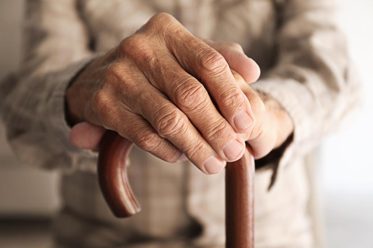 Close-up of elderly hands holding a cane — a symbol of longevity, wisdom, and lived experience in Greek culture