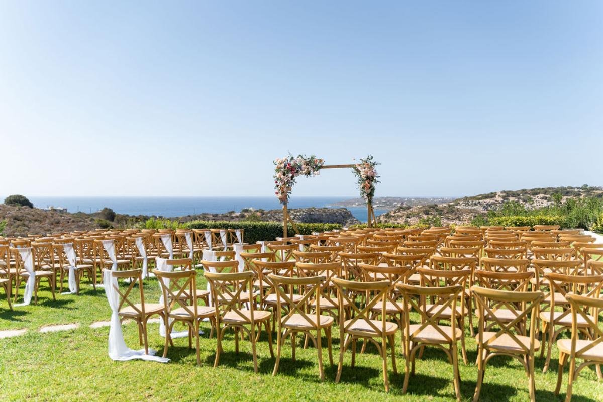 Rustic outdoor wedding ceremony in Crete overlooking the sea, with rows of wooden chairs