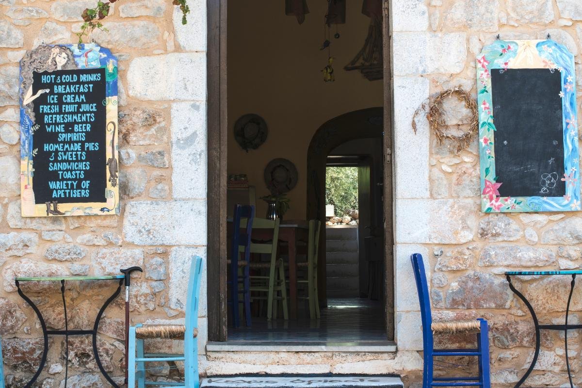 Inviting entrance to a traditional taverna in a Greek village, framed with chalkboard menus and rustic stone walls
