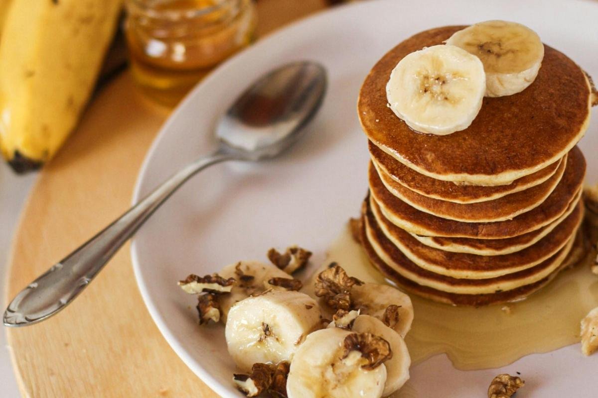 Stack of pancakes topped with Greek honey, banana slices, and walnuts