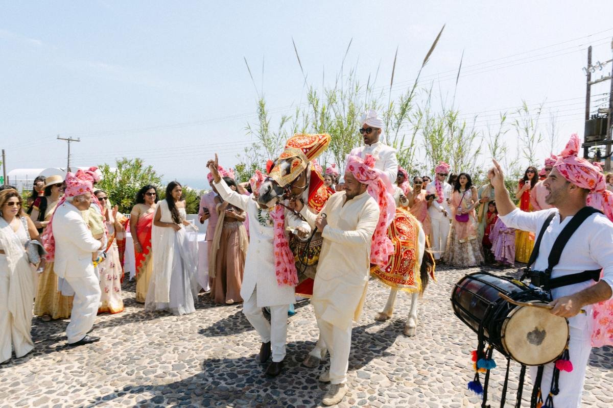 A hindu groom entering the wedding venue in santorini with a horse during baraat in a destination wedding in greece