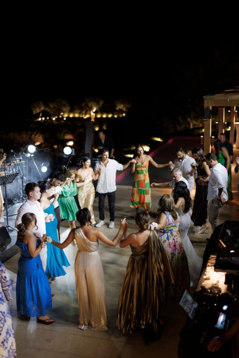 Guests dancing in a circle at a lively outdoor Greek wedding reception