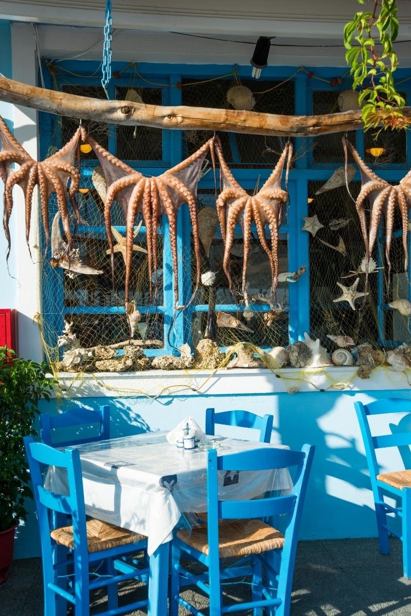A traditional blue-and-white Greek taverna in Thessaloniki with sun-dried octopus hanging outside, reflecting local food culture.